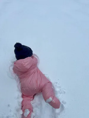 A toddler in a pink snowsuit face down in fresh snow