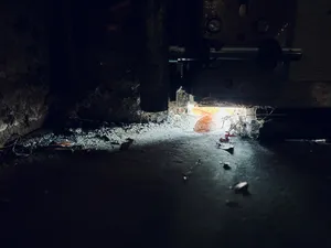 The small gap at the corner of a garage door letting brilliant sunlight onto a narrow slice of a dark, dirty garage floor