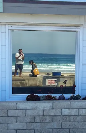 Andrew and Theresa reflected in a window with the ocean in the background