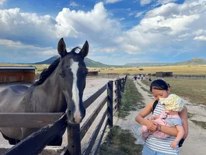 Theresa holding the baby across from a black horse in a paddock