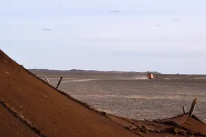 An orange van receding in the desert seen from a Berber hut